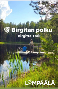 Kuva: Birgitan polku – Birgitta Trail Maisemakuva laiturilta metsälammen rannalla. Kaksi henkilöä istuu ja seisoo laiturilla veden äärellä. Taustalla näkyy tiheä kuusimetsä ja sininen taivas. Kuvassa on tekstit Birgitan polku – Birgitta Trail sekä Lempäälä-logo alareunassa.