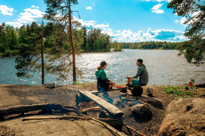 Kaksi ihmistä istuu Kirskaanniemen nuotiopaikalla järven äärellä.