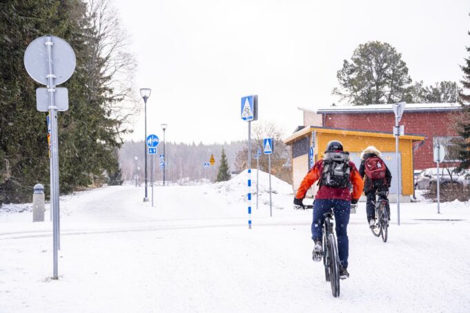 Kaksi pyöräilijää pyöräilee lumisessa maisemassa.