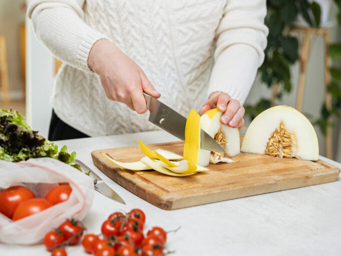 Ihminen leikkaa hedelmää puisella leikkuulaudalla. Kuvassa näkyy kädet.