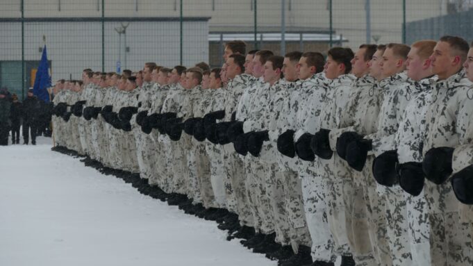 Joukko sotilaita seisoo rivissä ulkona talvella lumisessa maisemassa.