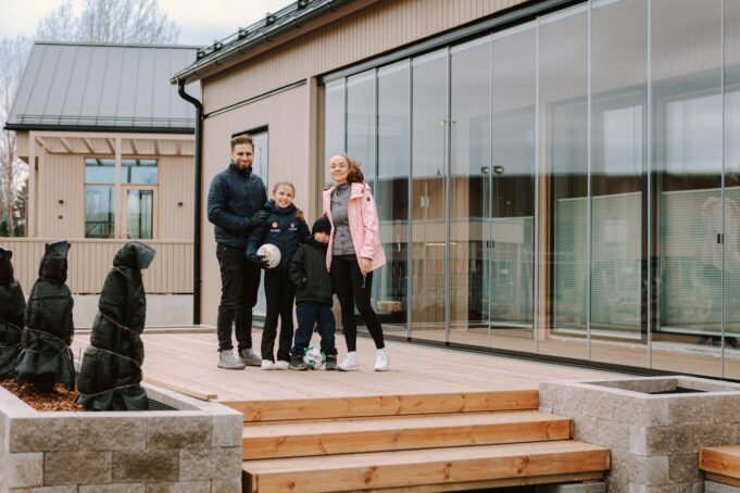 Lapsiperhe seisoo uuden talon ulkoterassilla ja katsoo kameraan.