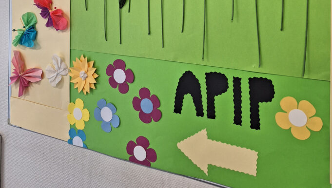 Seinällä pahvinen taulu, jossa on kukkakoristeita ja lukee apip.