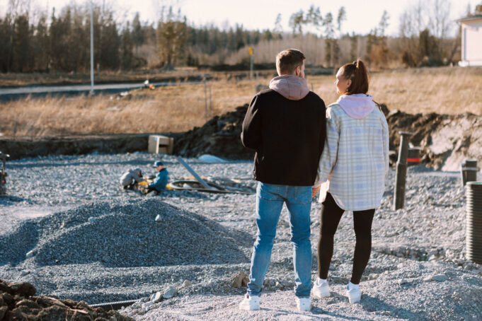 Pariskunta seisoo Humalamäessä tontin laidalla ja katsoo tonttia, jossa lapset leikkivät.