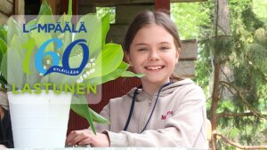 Lapsi istuu pöydän ääressä ulkotilassa. Etualalla on valkovuokkoja sisältävä ruukku. Kuvassa näkyy teksti ”Lempäälä 160 kylillään – Lastunen”.