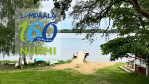 Lempäälä 160 kylillään ‑juhlateemainen kansikuva Nurmelta, järvi ja laituri.´, vihreä nurmikko ja lehtipuita