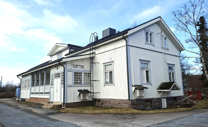Valkoinen puurakennus kuvattuna ulkoa pilvisessä säässä.