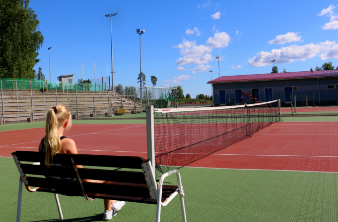 Tyttö penkillä tenniskentän laidalla