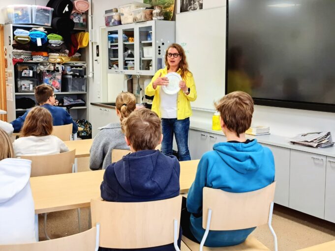 Opettaja seisoo luokan edessä ja puhuu oppilaille.