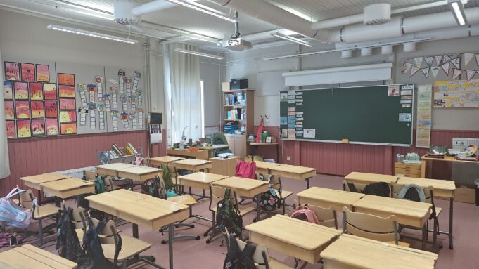 Kuokkalan koulun luokassa on pulpetteja sekä arkisia askarteluita.