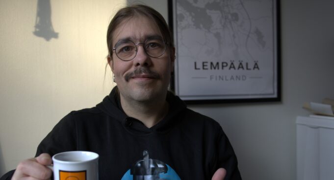 Niilo22 istuu kahvikuppi kädessä ja näyttää peukkua.